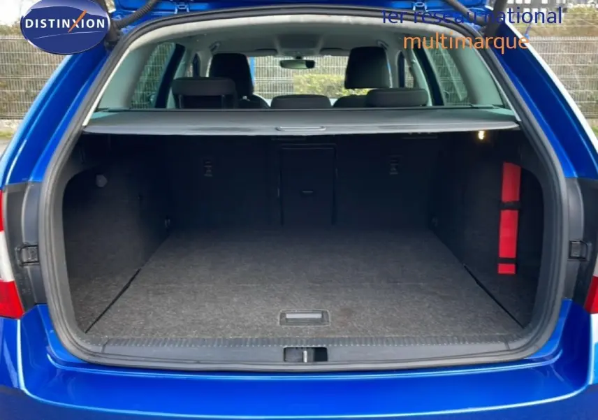 Coffre ouvert vu de l'arrière d'une Skoda Octavia Combi bleu racing metal, intérieur spacieux et tapis gris.