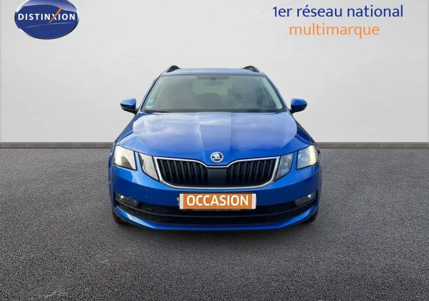 Vue frontale d'une Skoda Octavia Combi bleu racing métal, avec calandre noire et phares allumés sur fond neutre.