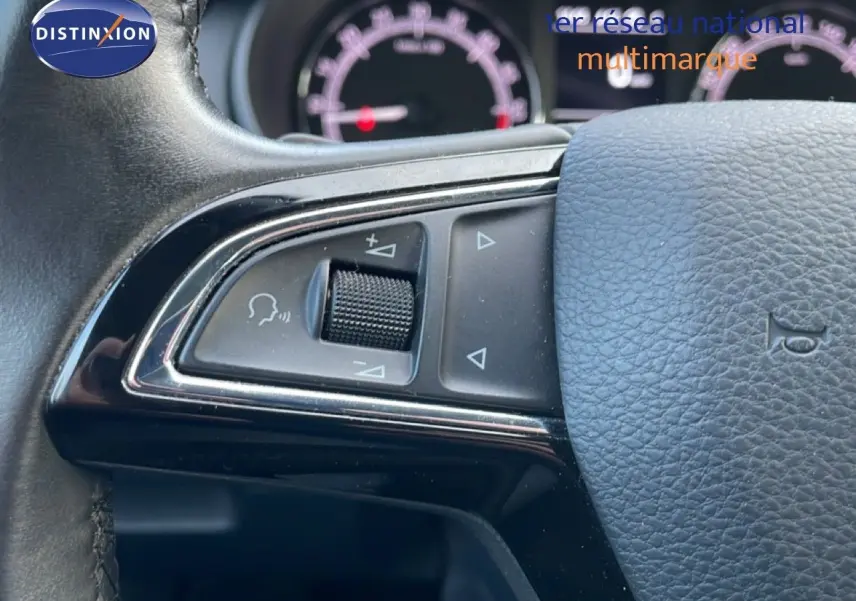 Gros plan sur les commandes gauche du volant en cuir noir de la Skoda Octavia Combi 2019, tableau de bord flou en arrière-plan.
