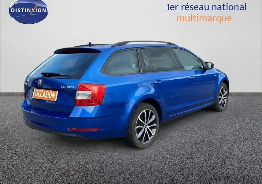 Vue 3/4 arrière droite d'une Skoda Octavia Combi 2019 bleu racing metal avec jantes alliage et barres de toit.