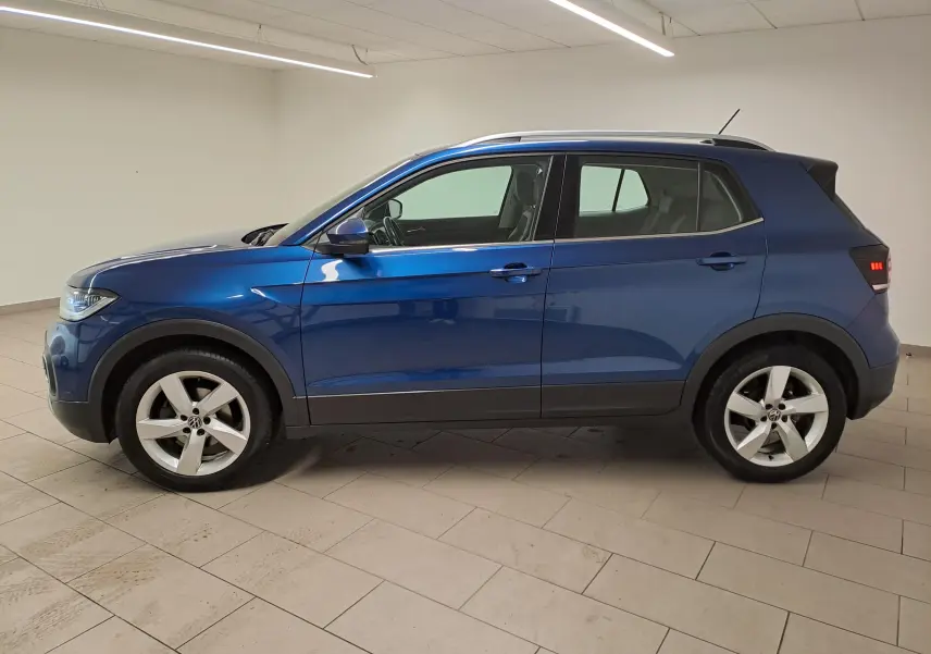 Profil côté gauche du Volkswagen T-Cross 2022 bleu récif avec jantes alliage et feux arrière allumés en intérieur.