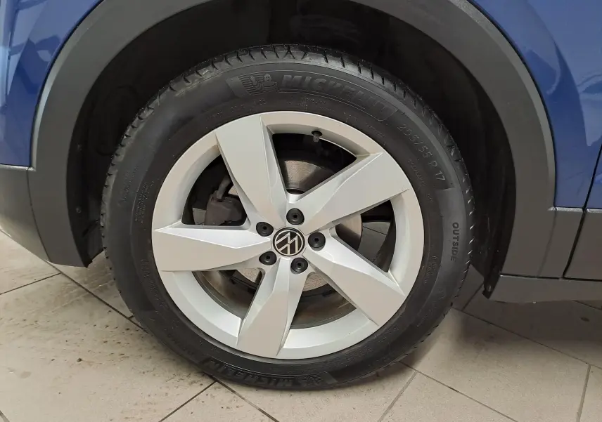 Gros plan sur la roue avant gauche d'un Volkswagen T-Cross bleu récif avec jante alliage cinq branches.
