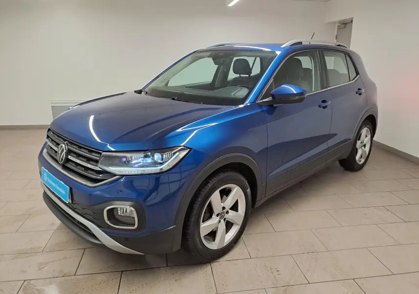 Volkswagen T-Cross Bleu Récif en 3/4 avant droit, avec phares allumés et jantes alliage cinq branches.