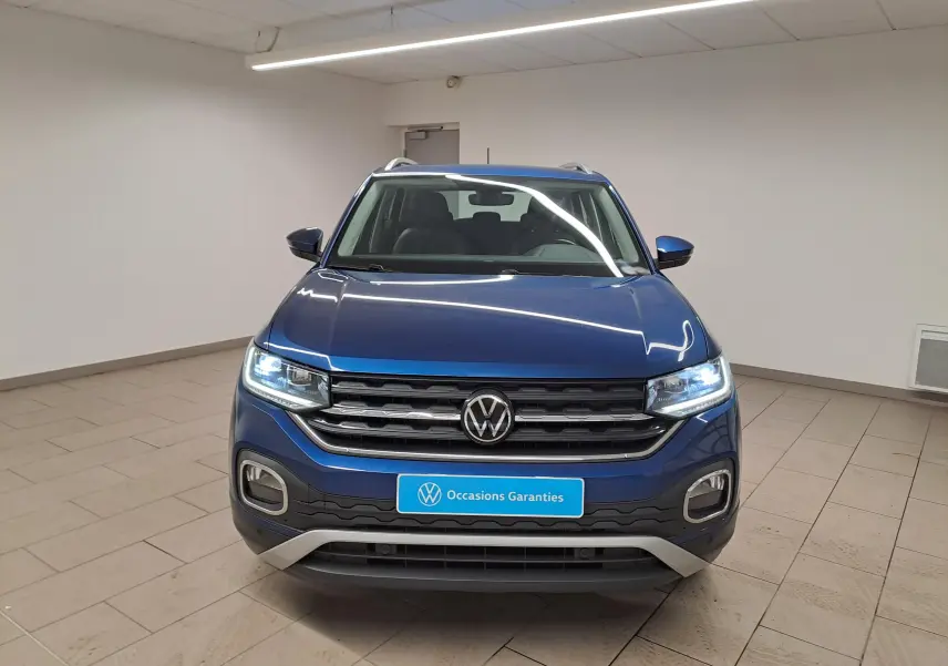 Vue frontale d'un Volkswagen T-Cross 1.0 TSI 110 DSG7 Style bleu récif avec phares allumés en intérieur.