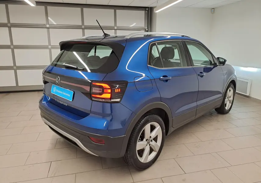 Volkswagen T-Cross Bleu Récif en 3/4 arrière droit, avec feux arrière allumés dans un garage.