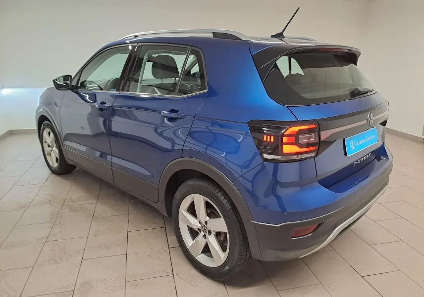 Vue 3/4 arrière droit du Volkswagen T-Cross bleu récif 2022 avec feux arrière allumés et jantes alliage cinq branches.