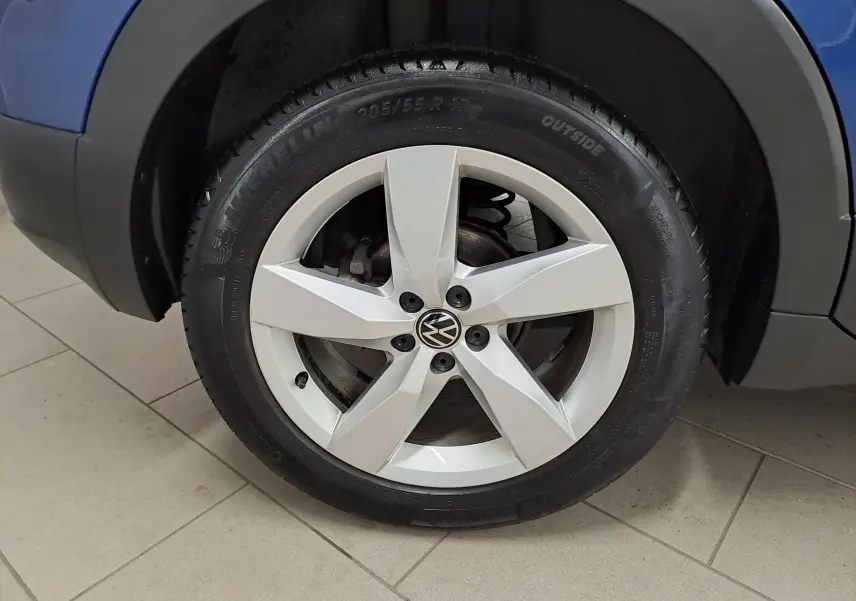 Gros plan sur la roue avant gauche du Volkswagen T-Cross bleu Récif, jante alliage cinq branches argentées.