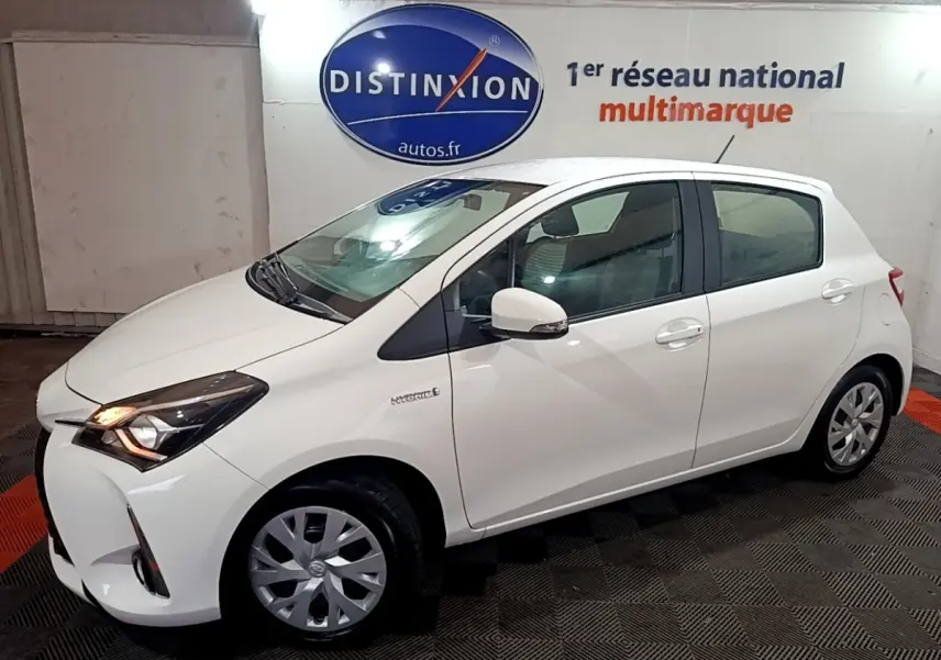 Toyota Yaris hybride blanche vue de profil côté gauche, avec phares allumés et jantes alliage simples.