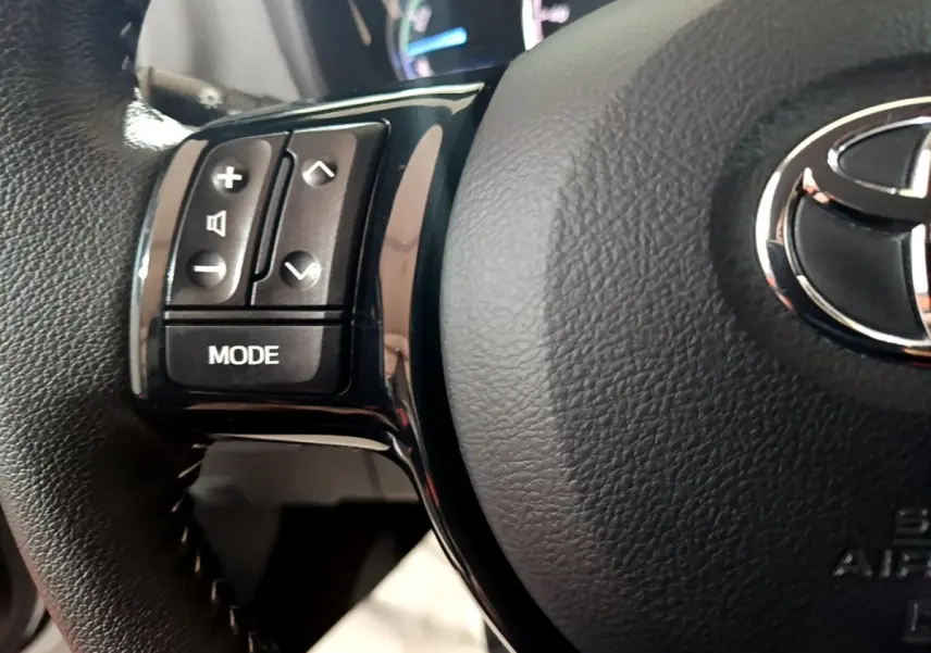 Gros plan sur le volant cuir noir de la Toyota Yaris 1.5 Hybrid, avec commandes audio et logo Toyota central argenté.