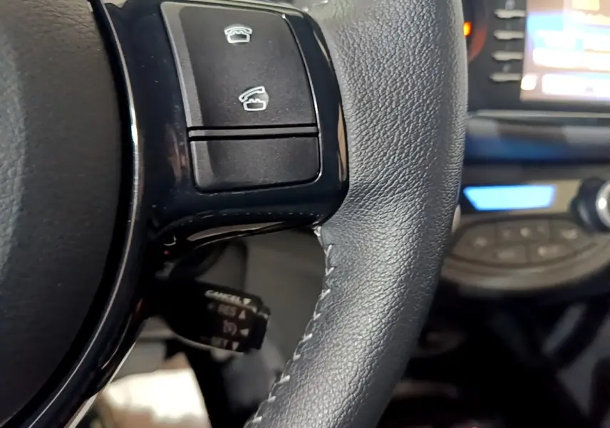 Gros plan sur le volant en cuir noir de la Toyota Yaris hybride 2019, avec commandes intégrées et tableau de bord flou en arrière-plan.