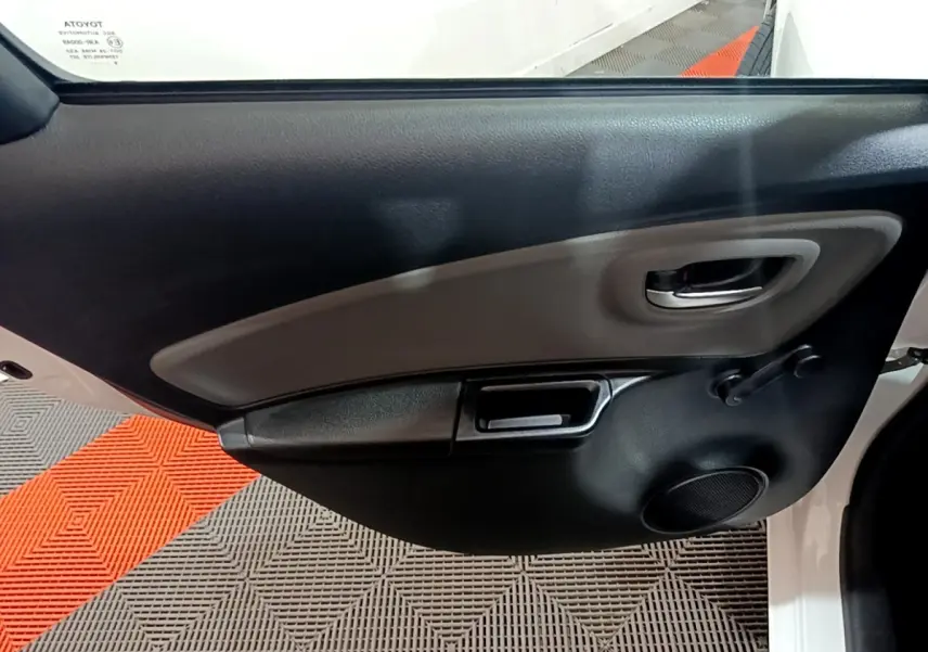 Gros plan sur la porte intérieure côté gauche de la Toyota Yaris blanche, montrant la poignée et le haut-parleur.