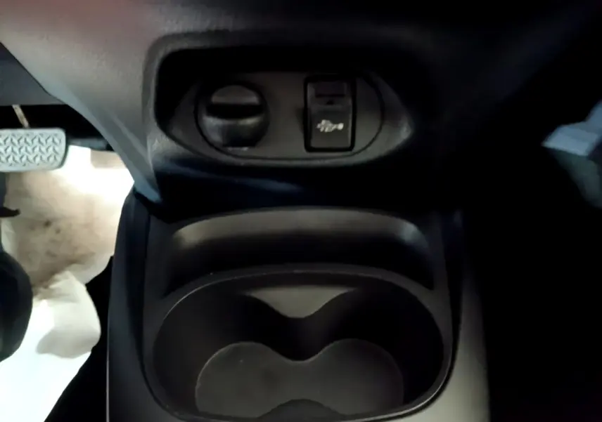 Gros plan sur le compartiment porte-gobelets et commande d'ouverture du capot dans l'habitacle d'une Toyota Yaris blanche 2019.