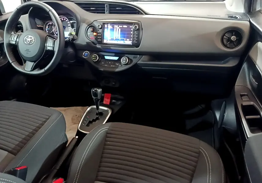 Vue intérieure avant droite de la Toyota Yaris 2019, tableau de bord noir avec écran tactile et sièges tissu gris foncé.