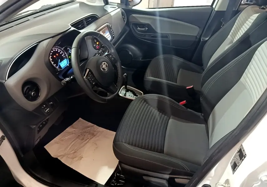 Intérieur avant droit de Toyota Yaris blanc 2019, sièges bicolores, volant cuir multifonctions et tableau de bord digital.