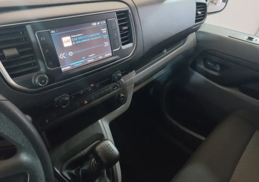 Vue intérieure côté passager du tableau de bord gris clair du Peugeot Traveller avec écran tactile et levier de vitesses manuel.