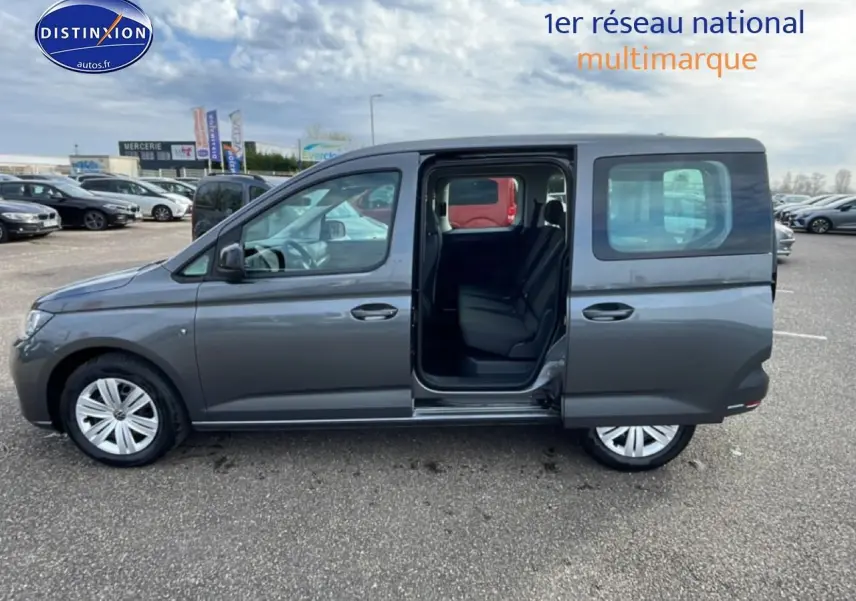 Vue de profil côté gauche d'un Volkswagen Caddy gris indien 2025 avec porte coulissante arrière ouverte montrant l'intérieur.