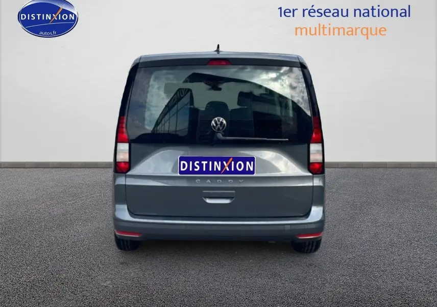Vue arrière d'un Volkswagen Caddy gris indien 2025 avec vitres teintées et logo VW visible.
