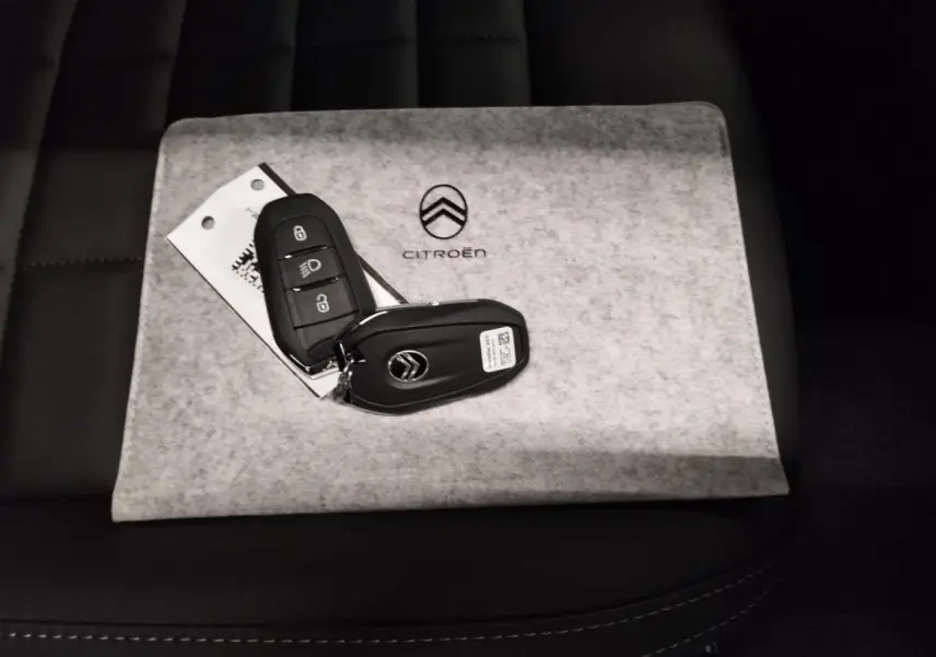 Clé de voiture Citroën posée sur un étui gris avec logo, sur siège noir en cuir, vue rapprochée intérieure.