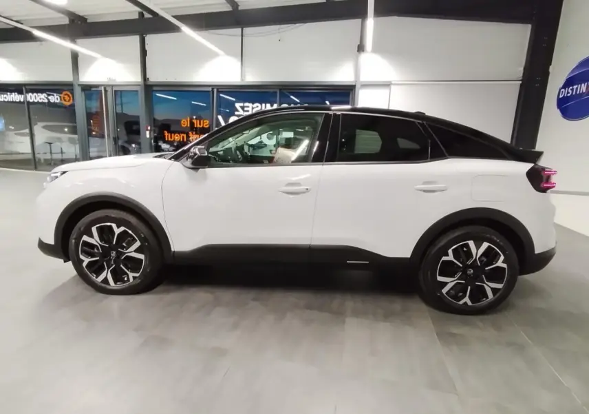 Vue de profil côté gauche d'une Citroën C4 blanche Okenite avec toit noir et jantes alliage 18 pouces en intérieur showroom.