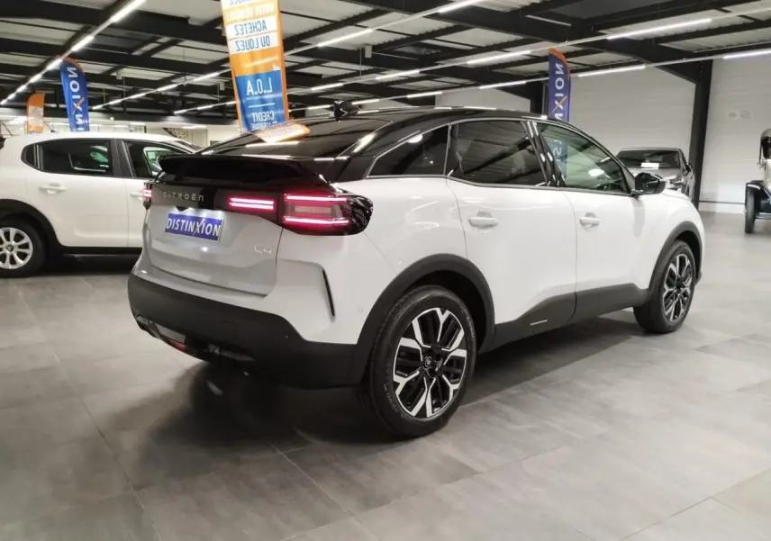 Vue 3/4 arrière droite d'une Citroën C4 blanche Okenite avec toit noir et jantes alliage 18'' dans un showroom.
