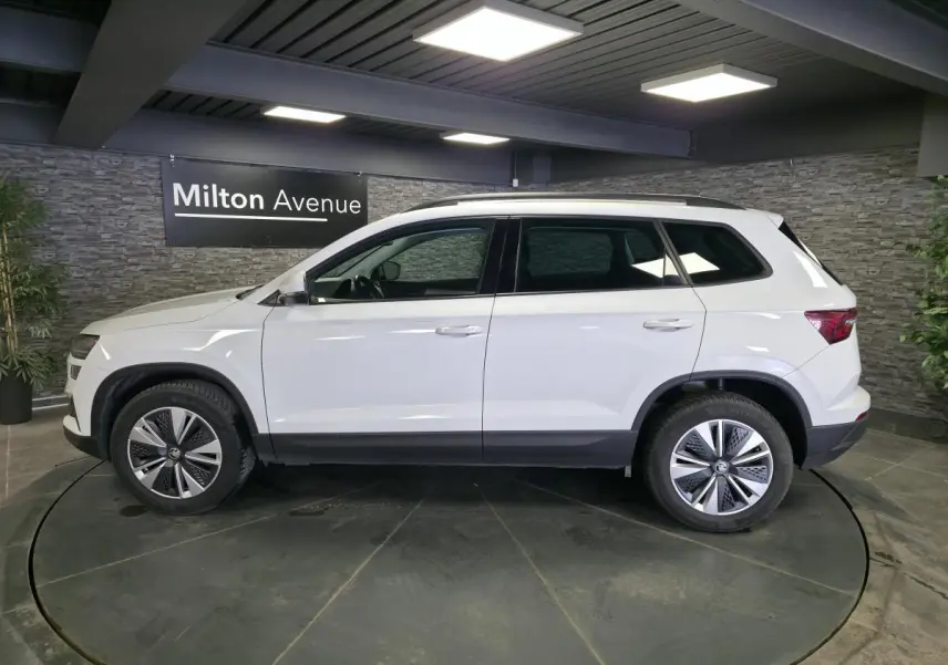Vue latérale droite d'un Skoda Karoq blanc 2023 avec jantes alliage 17'' et barres de toit noires.