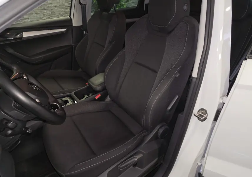 Vue intérieure côté gauche du Skoda Karoq blanc 2023, sièges avant noirs avec coutures contrastées et volant cuir.