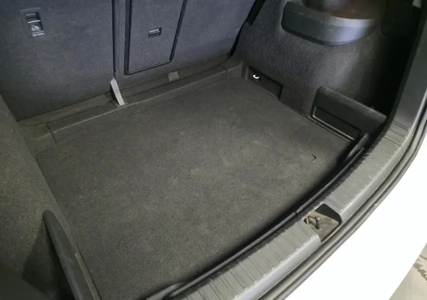 Coffre ouvert vu de dessus d’un Skoda Karoq blanc 2023, avec tapis de sol noir et compartiments latéraux.
