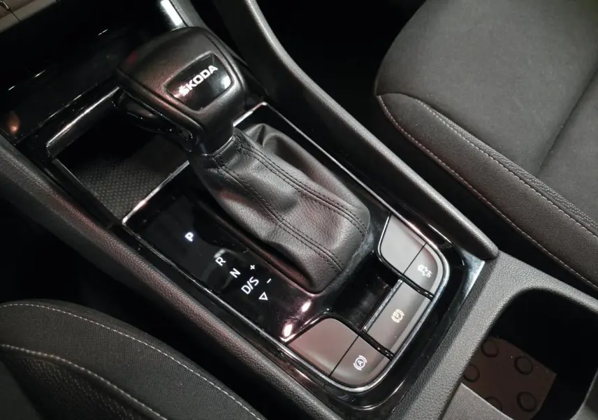 Gros plan sur le levier de vitesses automatique noir en cuir avec logo ŠKODA, entouré de commandes dans l'habitacle sombre.