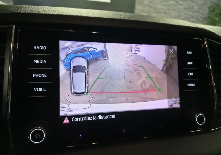 Écran de caméra de recul montrant une Skoda Karoq blanche vue de dessus en stationnement arrière.