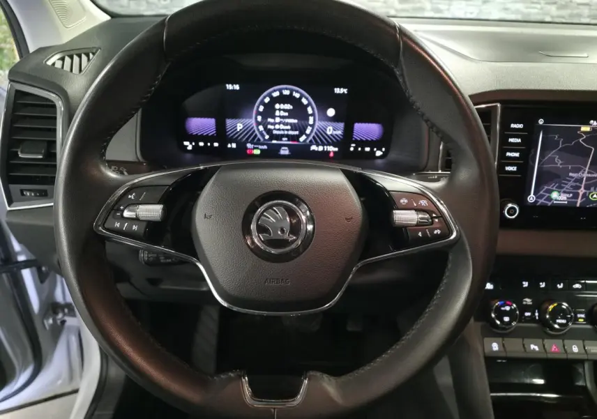 Vue rapprochée du volant cuir noir et du tableau de bord numérique du Skoda Karoq blanc 2023, affichage navigation visible.