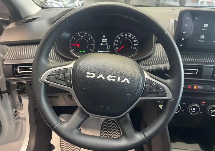 Vue intérieure centrée sur le volant noir DACIA avec tableau de bord et écran tactile du Sandero blanc 2024.