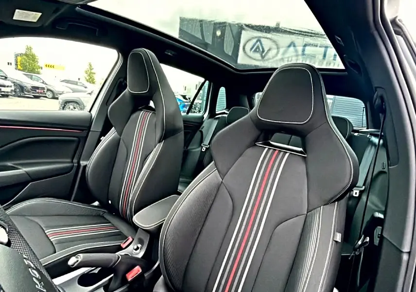 Vue intérieure des sièges avant sport noirs avec surpiqûres blanches et bandes rouges du Skoda Kamiq Monte Carlo 2026, toit panoramique visible.