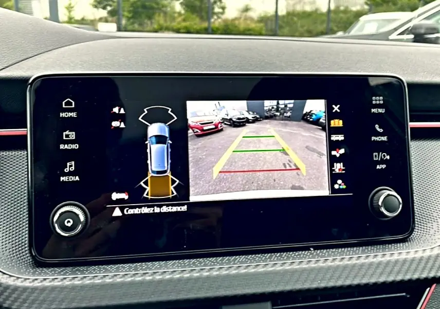 Écran tactile intérieur montrant la caméra de recul et l’aide au stationnement du Skoda Kamiq blanc nacré, vue de face.