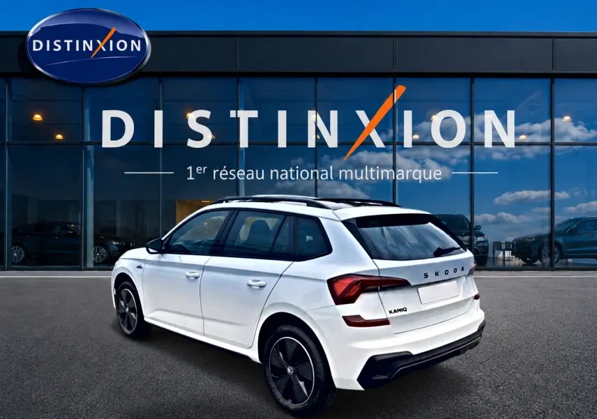 Vue 3/4 arrière droite d'un Skoda Kamiq blanc nacré avec jantes noires, garé devant une vitrine Distinxion.