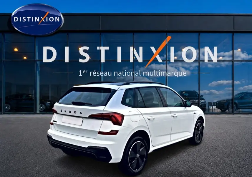 Vue 3/4 arrière droite d'un Skoda Kamiq blanc nacré avec jantes noires, devant une vitrine Distinxion.