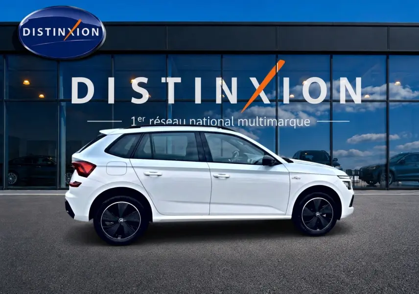 Vue latérale droite d'un Skoda Kamiq blanc nacre avec jantes noires devant une vitrine Distinxion.