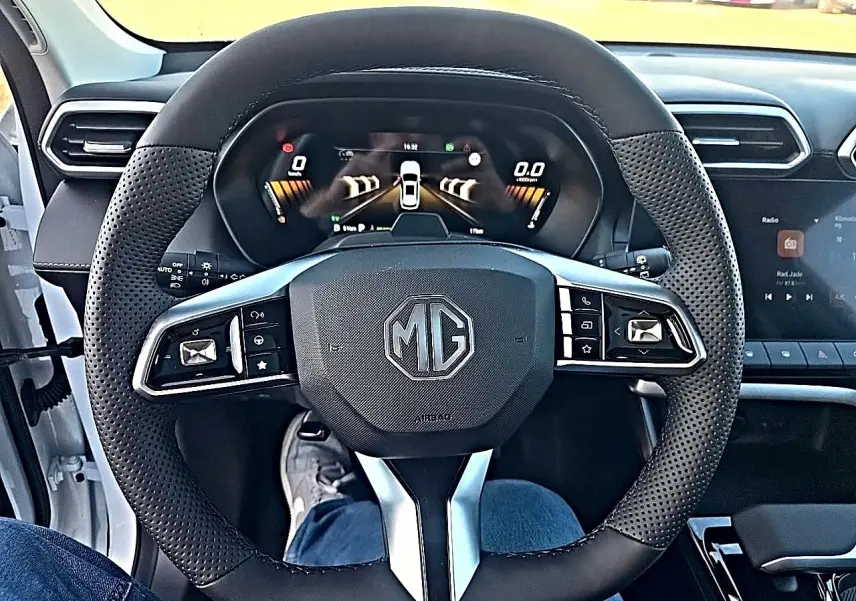 Vue intérieure centrée sur le volant multifonction noir perforé du MG ZS 1.5 hybrid 197 luxury avec tableau de bord digital.