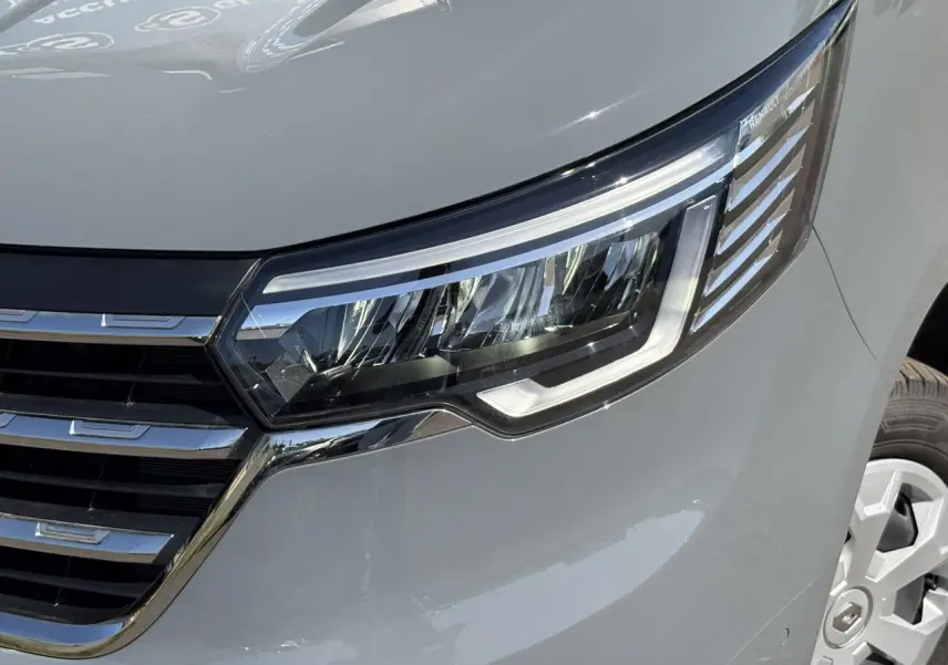 Gros plan sur le phare avant droit et la calandre chromée d'un Renault Trafic Fourgon Urban Grey 2024.