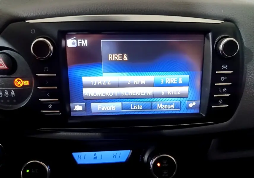 Écran tactile central de la Toyota Yaris hybride 2019 affichant les stations FM, avec commandes climatisation en dessous.