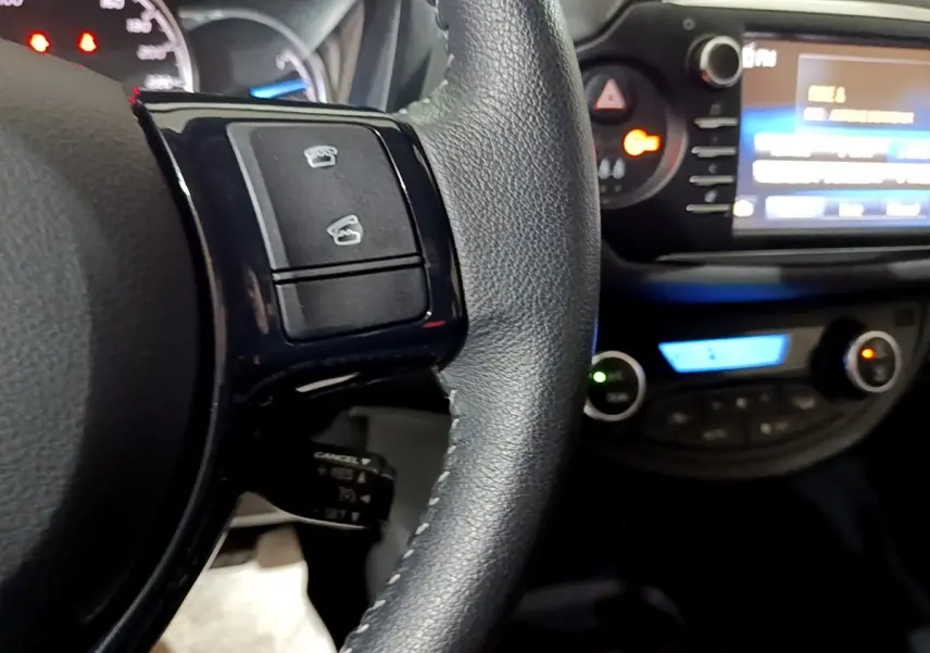 Gros plan sur le volant cuir noir de la Toyota Yaris 2019 avec commandes intégrées et tableau de bord éclairé.