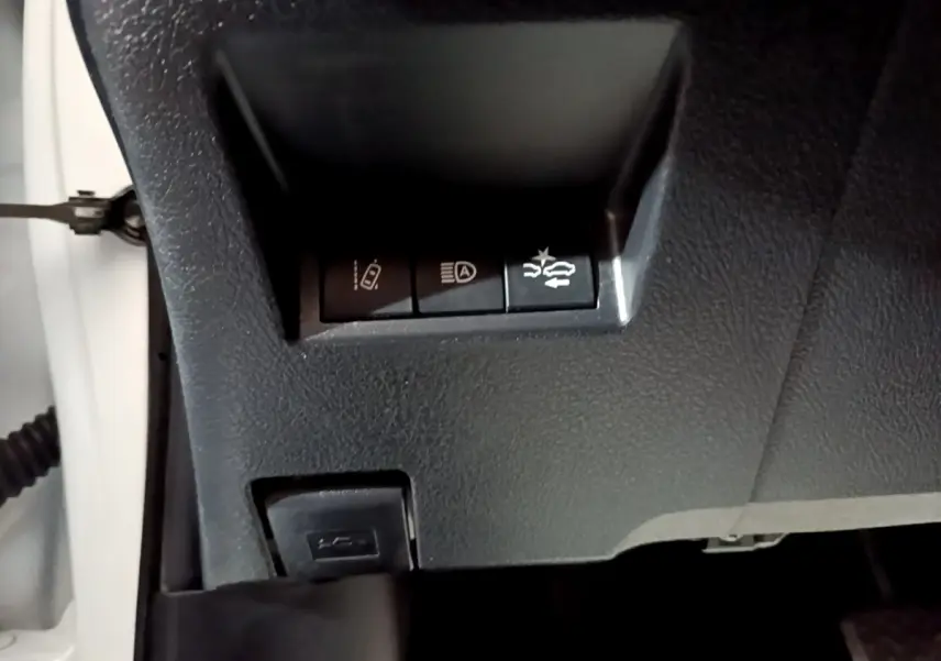 Gros plan sur les commandes de sécurité sous le tableau de bord d'une Toyota Yaris blanche hybride 2019.