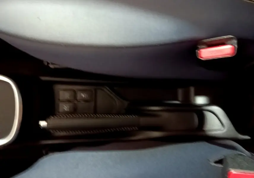 Vue rapprochée de la poignée de frein à main et des boutons de commande entre les sièges avant d'une Toyota Yaris blanche.