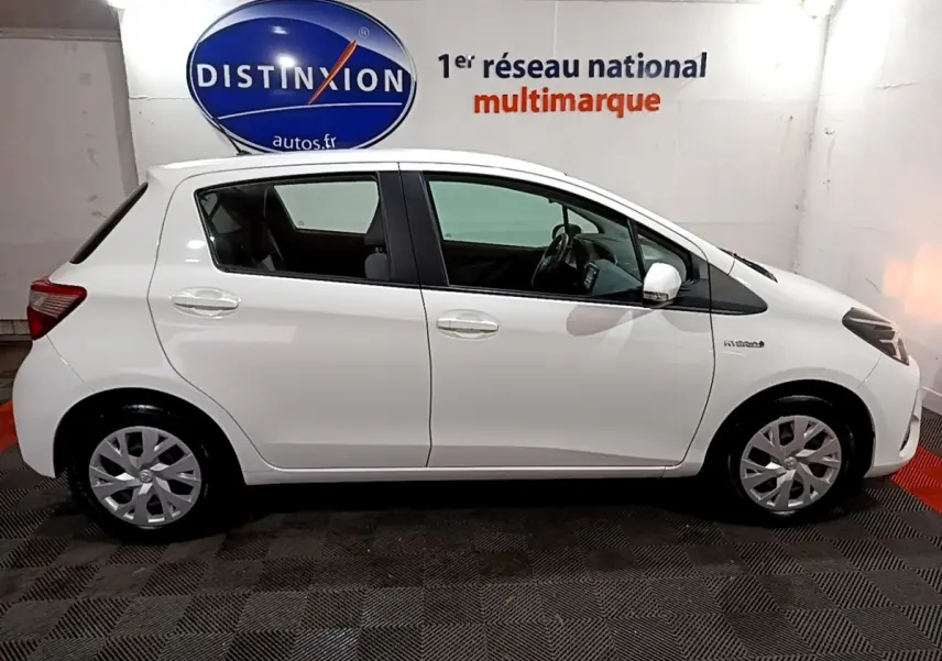 Profil droit d'une Toyota Yaris blanche 2019 hybride, avec jantes standard et logo Hybrid visible sur l'aile avant.