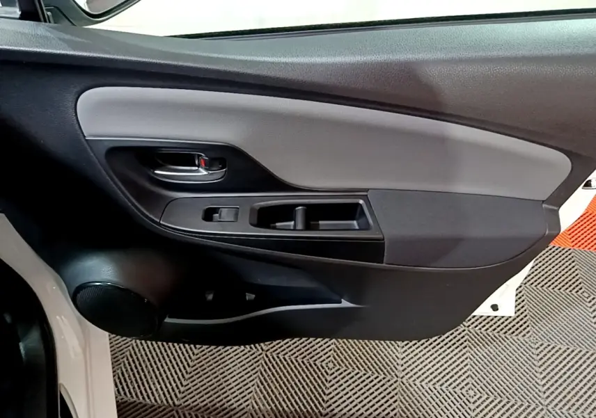 Gros plan sur la porte intérieure côté gauche d'une Toyota Yaris blanche, montrant la poignée et les commandes de fenêtre.