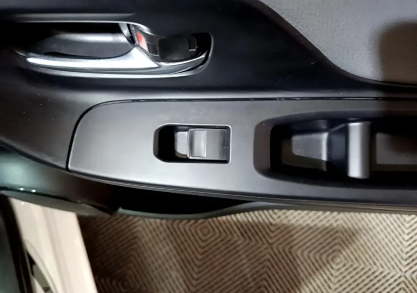 Gros plan sur la poignée intérieure et les commandes de lève-vitre côté conducteur d'une Toyota Yaris blanche 2019.