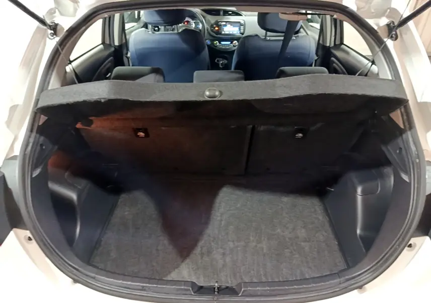 Coffre ouvert vu de l'arrière d'une Toyota Yaris blanche, intérieur noir avec tablette cache-bagages et sièges avant visibles.