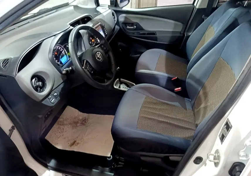 Intérieur côté conducteur d'une Toyota Yaris blanche 2019, montrant sièges tissu bleu et tableau de bord avec écran tactile.