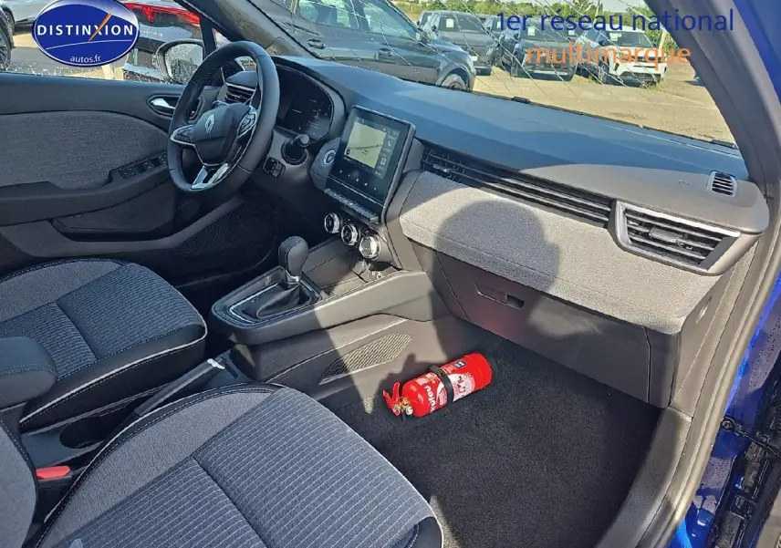 Vue intérieure côté passager de la Renault Clio V bleu iron, avec tableau de bord moderne et extincteur au sol.