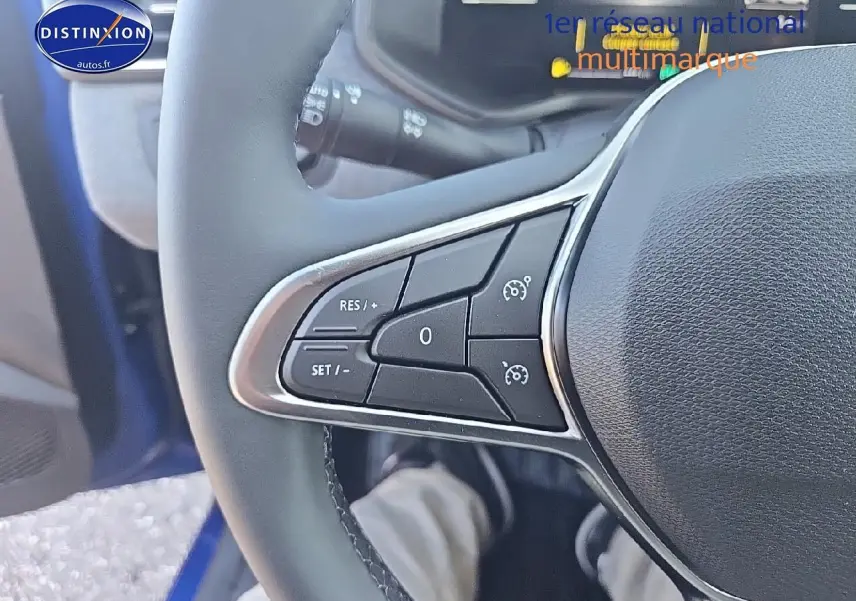 Gros plan sur les commandes de régulateur au volant d'une Renault Clio V bleu iron, côté gauche visible.