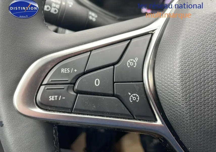 Gros plan sur les commandes du régulateur de vitesse au volant d'une Renault Clio V blanche, version 2025.